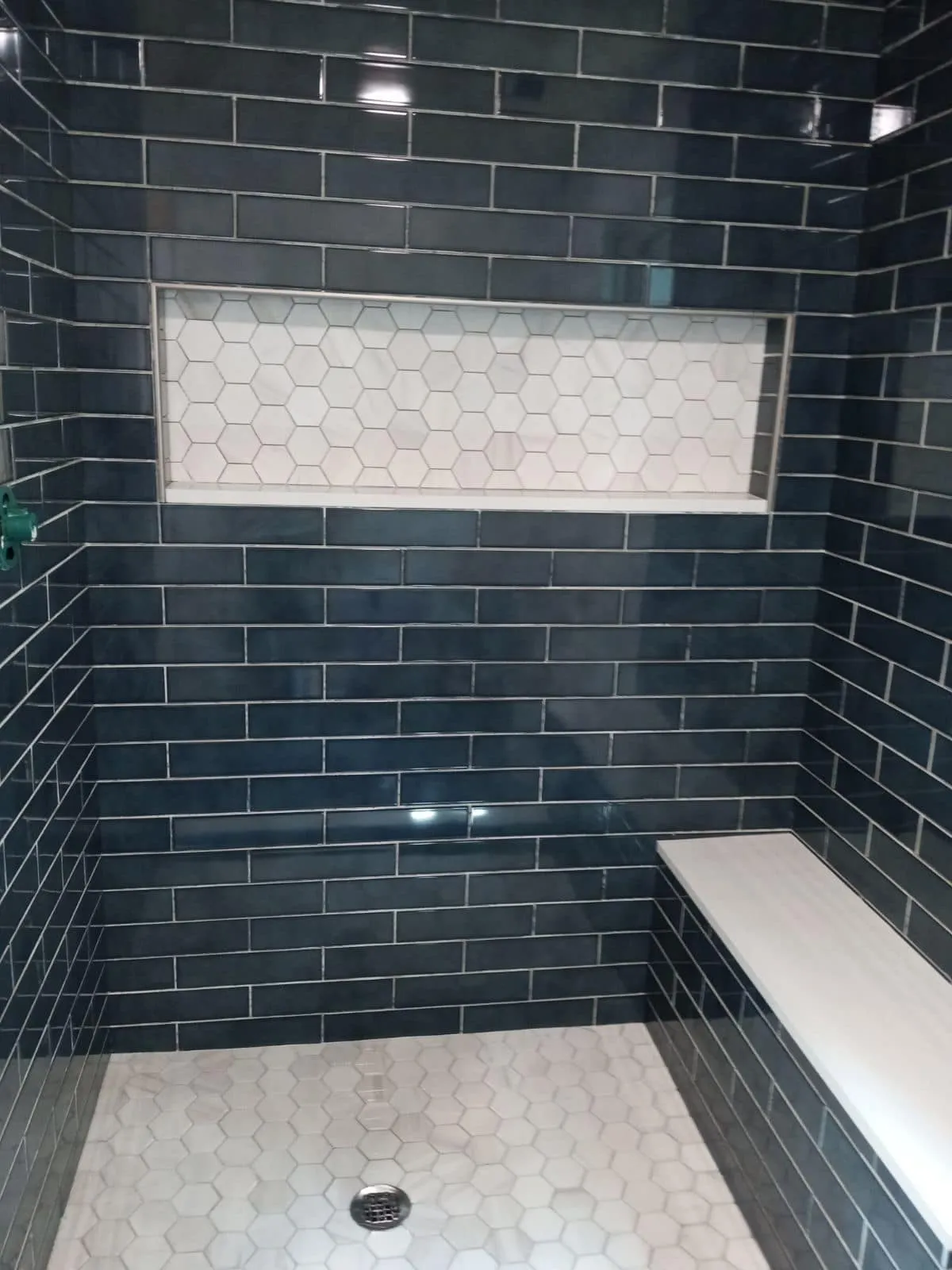 A navy tile shower with a bench and a long niche
