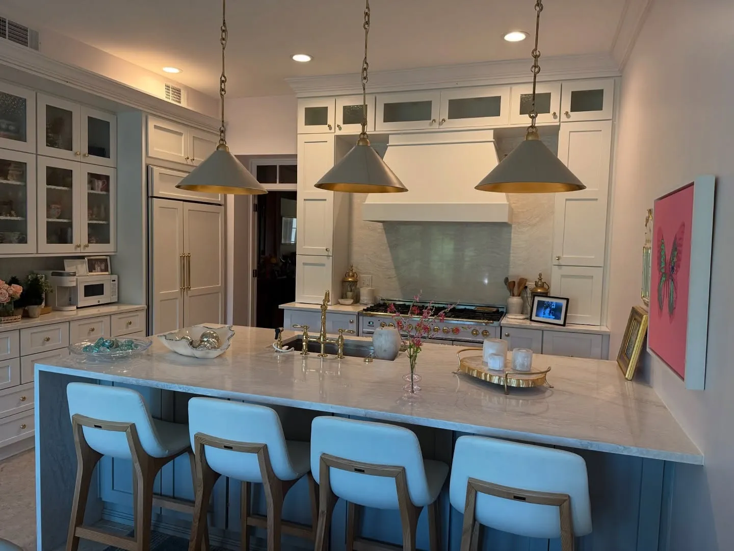 A white kitchen with a quartz waterfall island and brass pendants