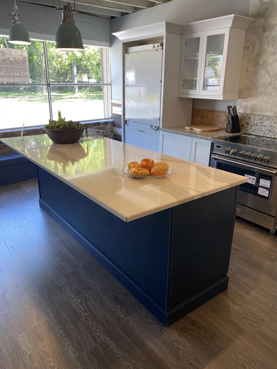 A finished kitchen with a navy island, white upper cabinets and a stainless range