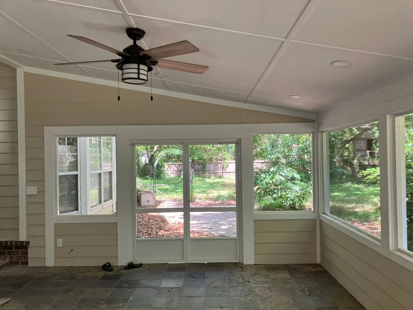 Inside a finished sunroom addition with a ceiling fan and windows onto the yard